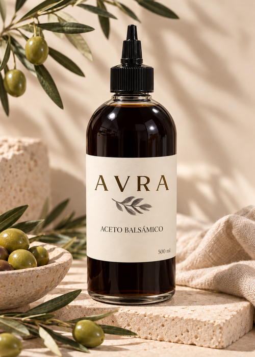 Botella de aceto balsámico AVRA de 500 ml con tapa dosificadora negra, junto a una rama de olivo y un bol de aceitunas